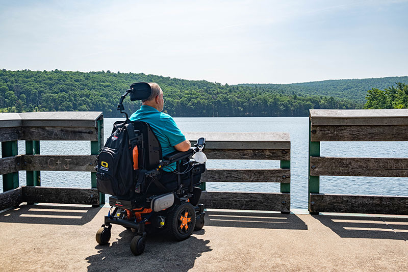 Man with motorized wheelchair sitting on fishing pier and looking at lake