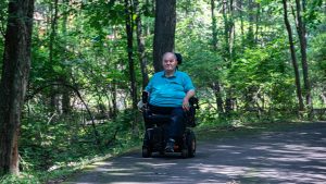 Man with motorized wheelchair on wooded walking trail
